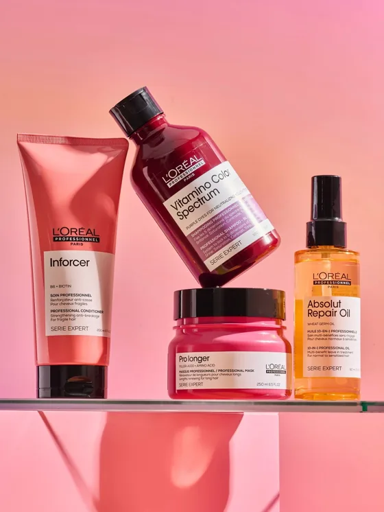Haircare bottles and tubes with printed labels on a pink shelf